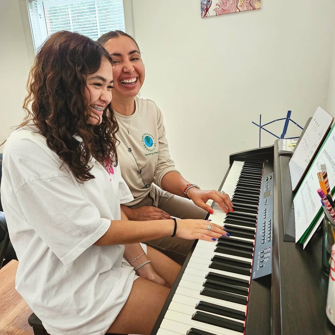 A piano student and her teacher laughing together at the keyboard